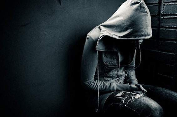 Person sitting against a wall with hood covering head and face