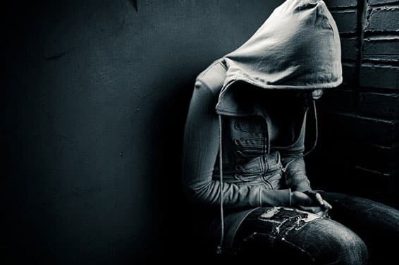 Person sitting against a wall with hood covering head and face
