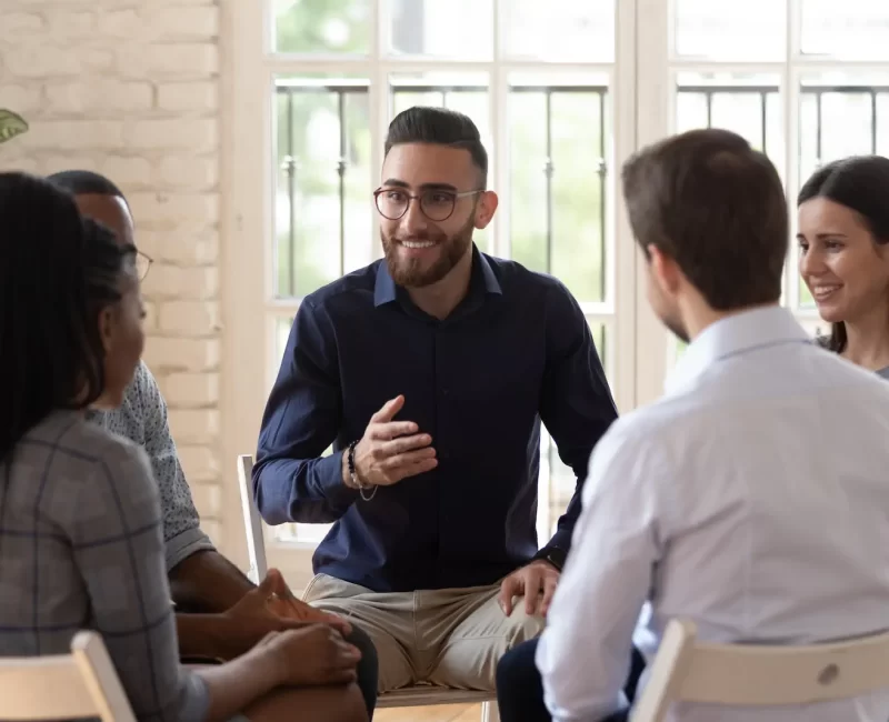 smiling-arabic-male-mentor-coach-sit-circle-with-diverse-patients-counseling-help-overcome-life-problems-multiethnic-young-people-share-thoughts-speak-psychological-therapy-session smiling-arabic-male-mentor-coach-sit-circle-with-diverse-patients-counseling-help-overcome-life-problems-multiethnic-young-people-share-thoughts-speak-psychological-therapy-session